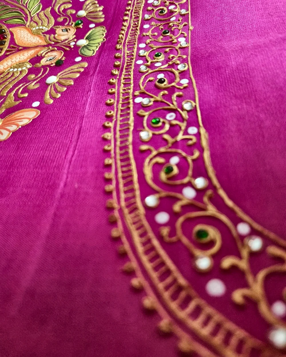 Close view of gold hand-painted detailing and stones on vivid pink fabric