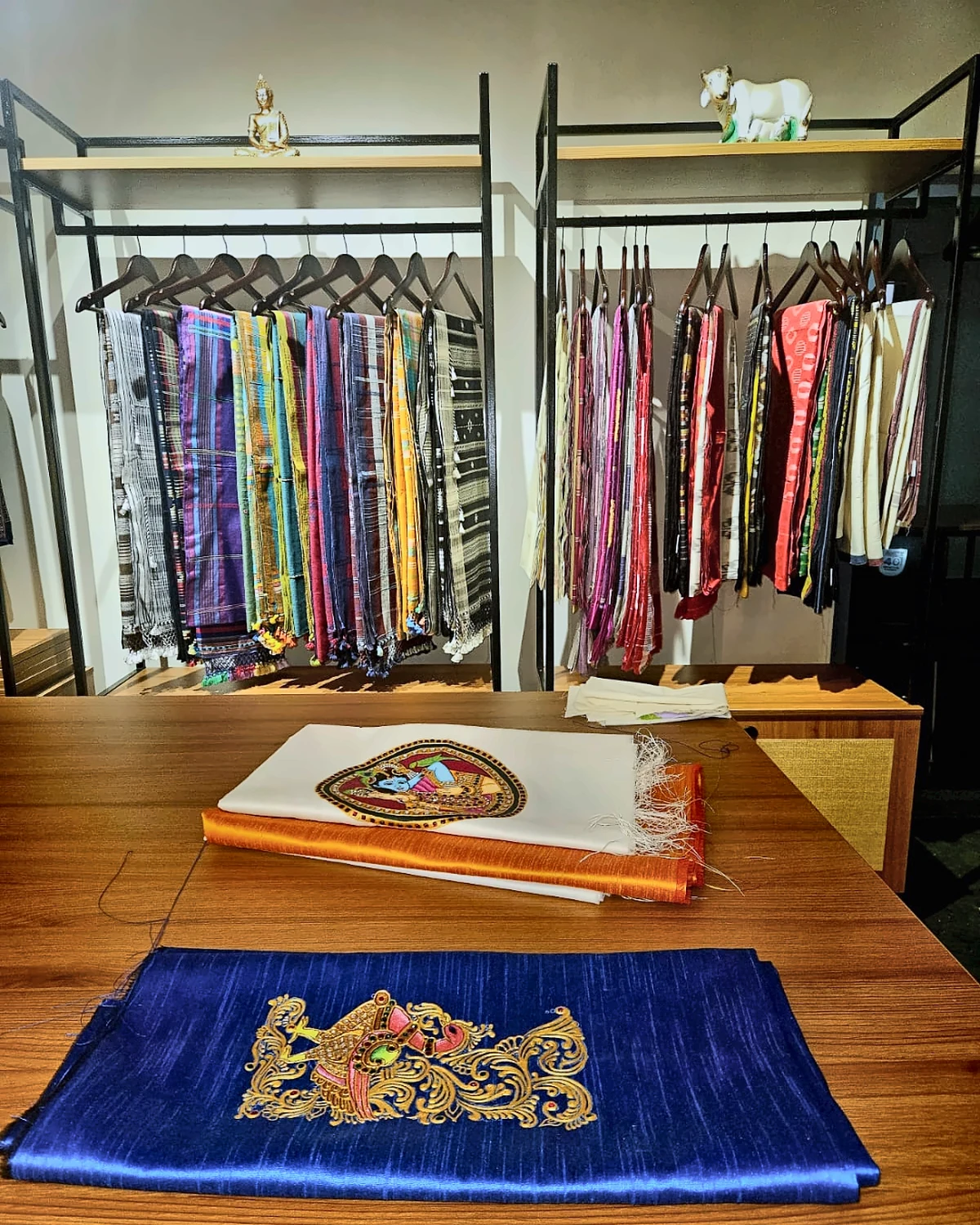 Handloom sarees displayed on studio racks behind a selection table with painted textiles